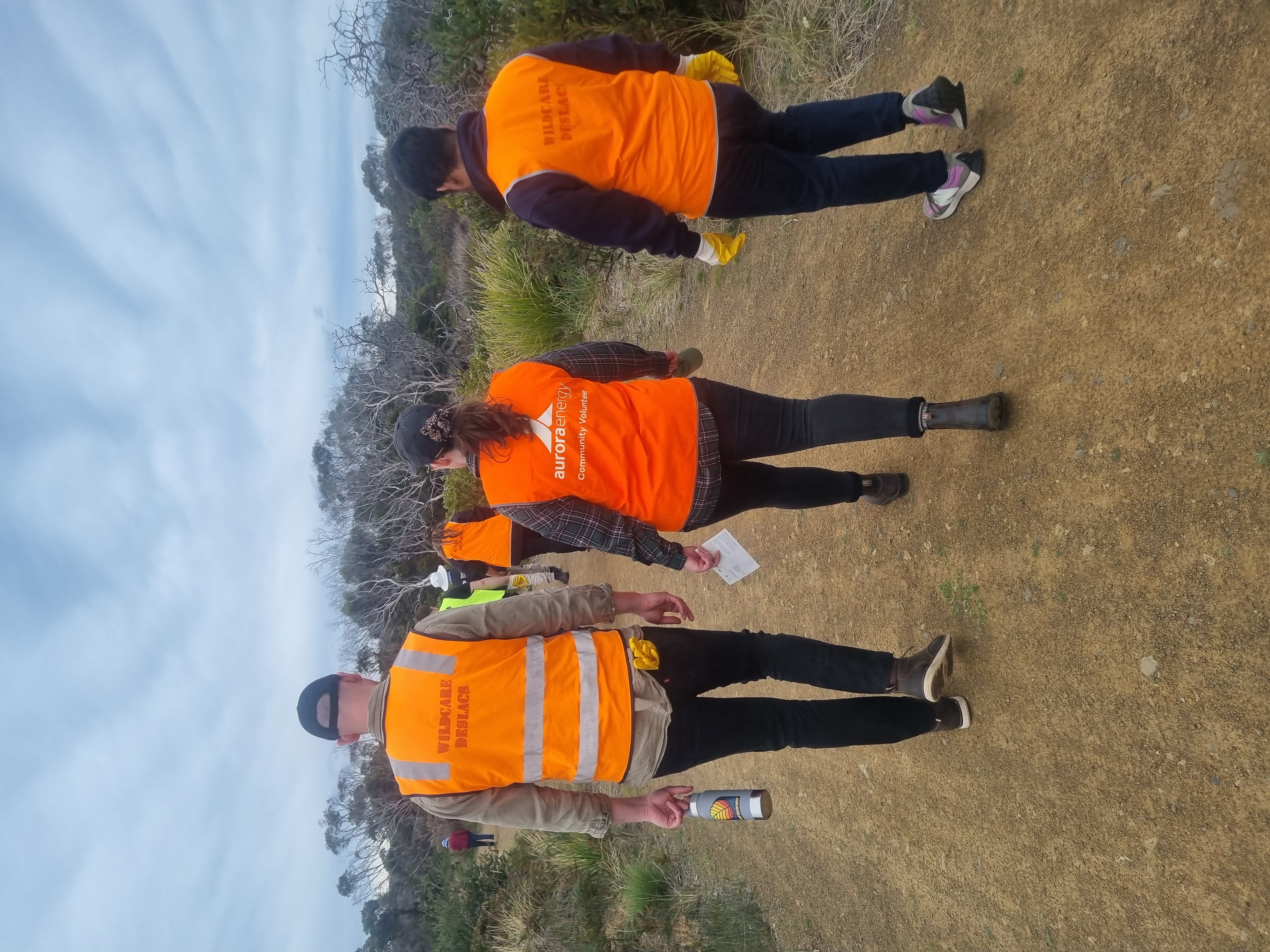 Three people in high vis vests walking down a dirt track